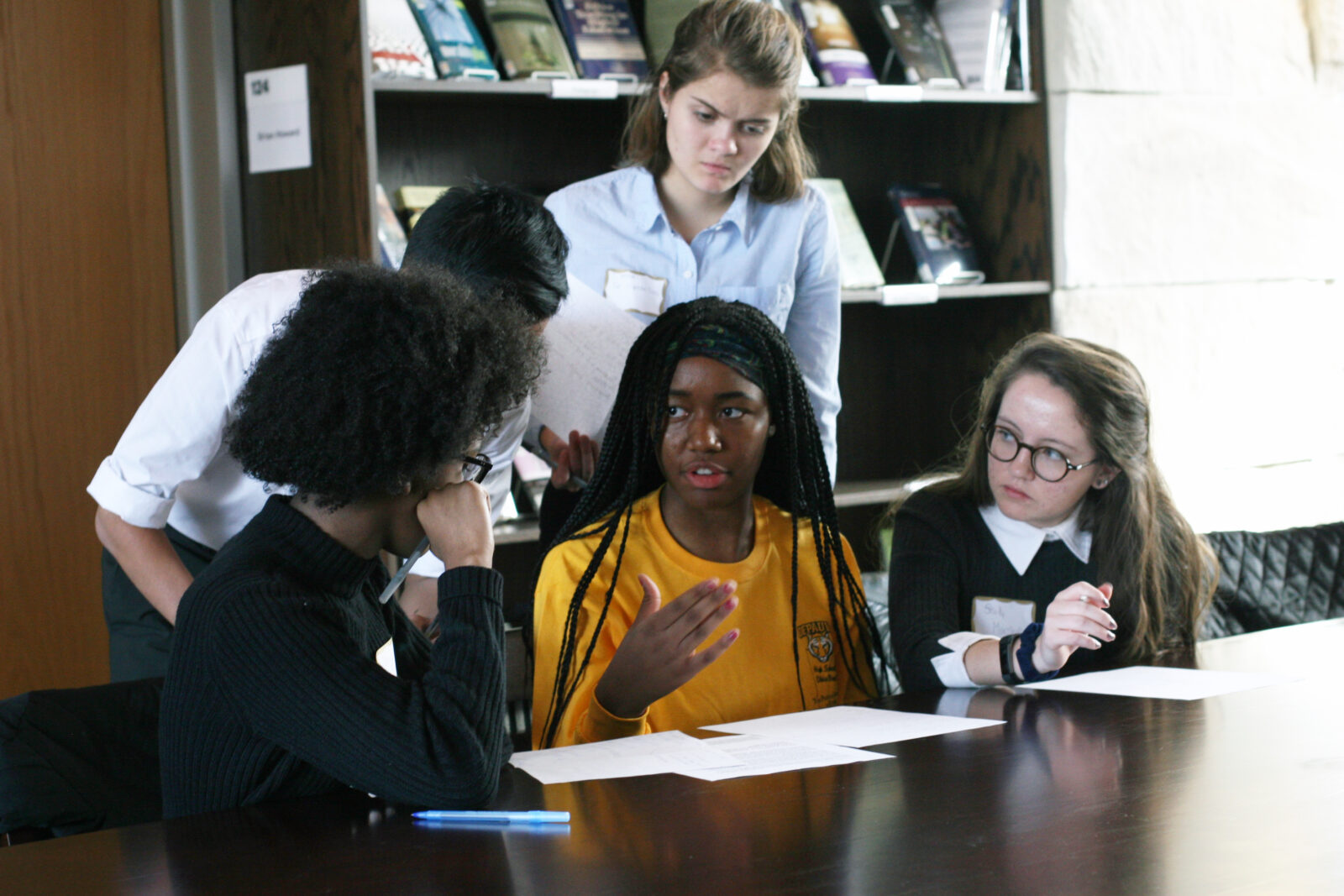 A diverse group of young people huddle in discussion in a library.