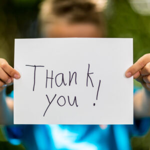 Blurred boy holding a piece of paper with the words Thank You in front of him.