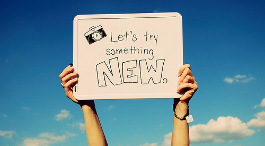 White board sign with drawing of camera and "Let's try something NEW."