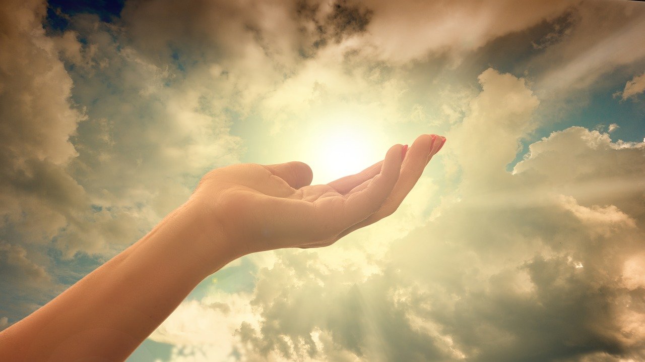 Hand appearing to hold sun with clouds in sky.